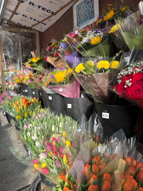 A wide view of a floral shop display with an array of fresh flowers arranged in black buckets and wrapped bouquets. The display includes vibrant tulips in shades of pink, orange, and yellow, alongside